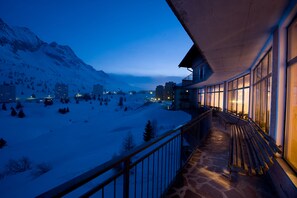 A snow-covered landscape with mountains in the background and a building with large windows and a balcony overlooking the scene. - Adamello (Vermiglio)