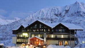 Un hotel de varios pisos con tejado nevado y balcones, rodeado de montañas cubiertas de nieve.