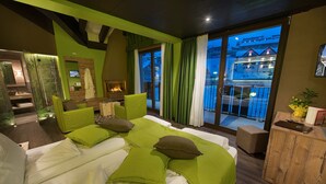 Una habitación de hotel moderna con una cama grande, ropa de cama verde, un armario de madera y un balcón con vistas.