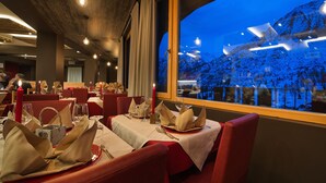 Un restaurante con mesas preparadas para comer, vista de una montaña nevada a través de amplios ventanales y un diseño de interiores moderno.