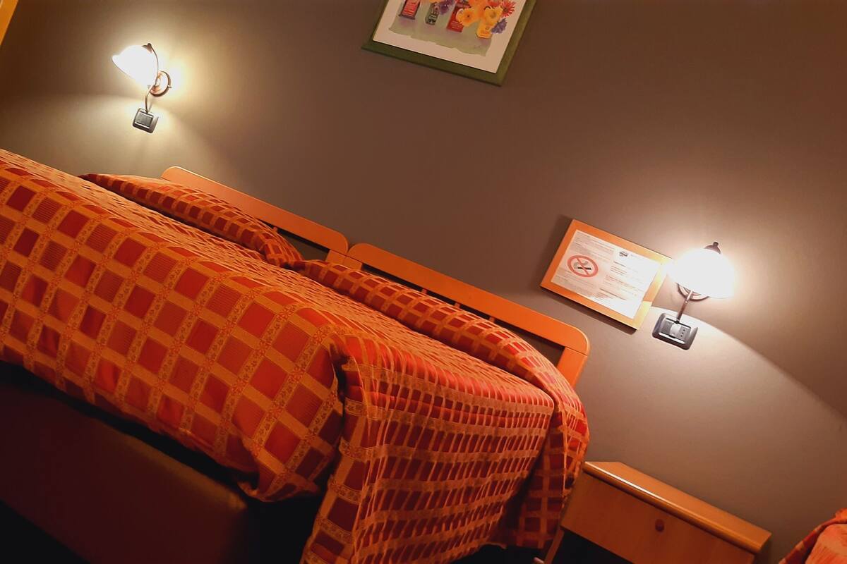 A hotel room with a long bed, two bedside tables, and two wall-mounted lamps.