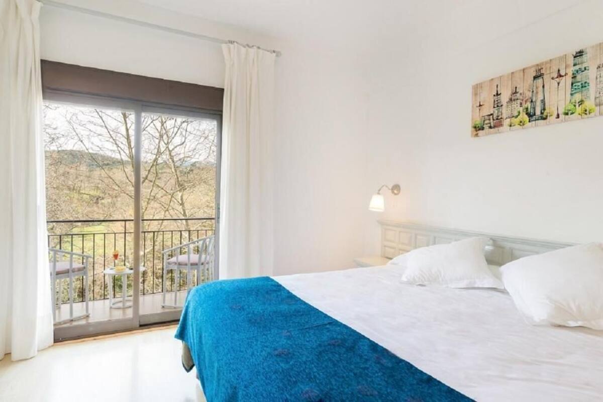 Quarto de hotel com uma cama, uma varanda com mesa e cadeiras, e um quadro na parede.