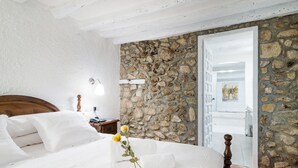 A bedroom with a stone wall, a wooden bed frame, a nightstand, and a white door leading to another room.