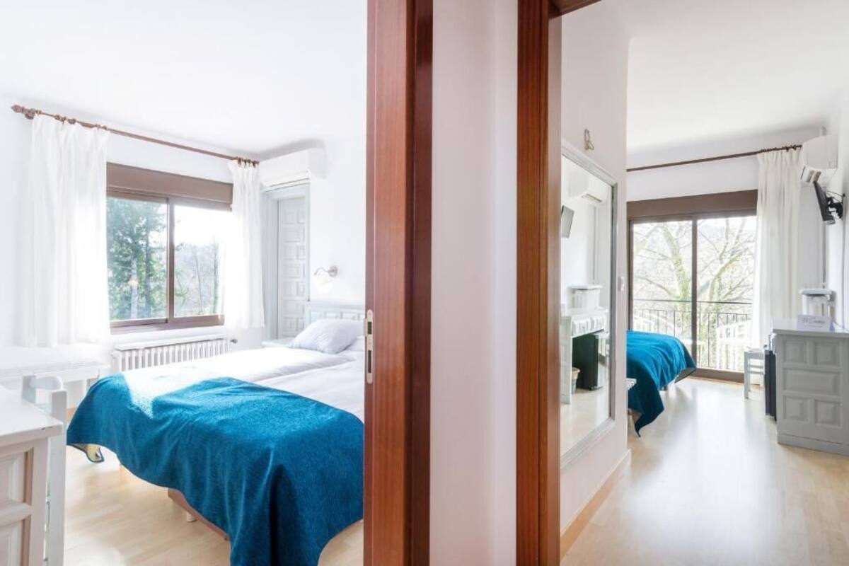 Quarto de hotel com duas camas, uma janela grande, um espelho e uma varanda.