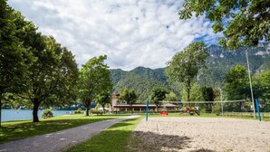 A park with a volleyball court, trees, and a lake in the background.