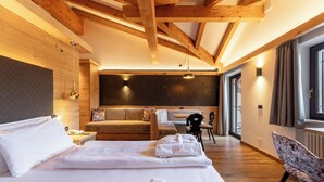 A spacious room with a large bed, a sofa, a dining table, and a chair. - Hotel Terme Antico Bagno (San Giovanni di Fassa)