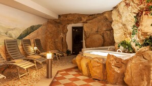 A spa area with a rock wall, a hot tub, and lounge chairs. - Hotel Terme Antico Bagno (San Giovanni di Fassa)