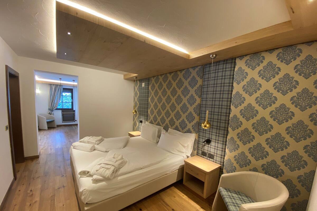 A modern bedroom with a large bed, bedside tables, a chair, and patterned wallpaper.