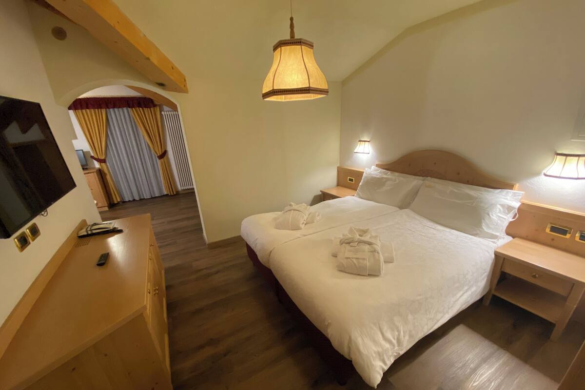 A hotel room with a bed, bedside tables, a TV, and a wooden floor.