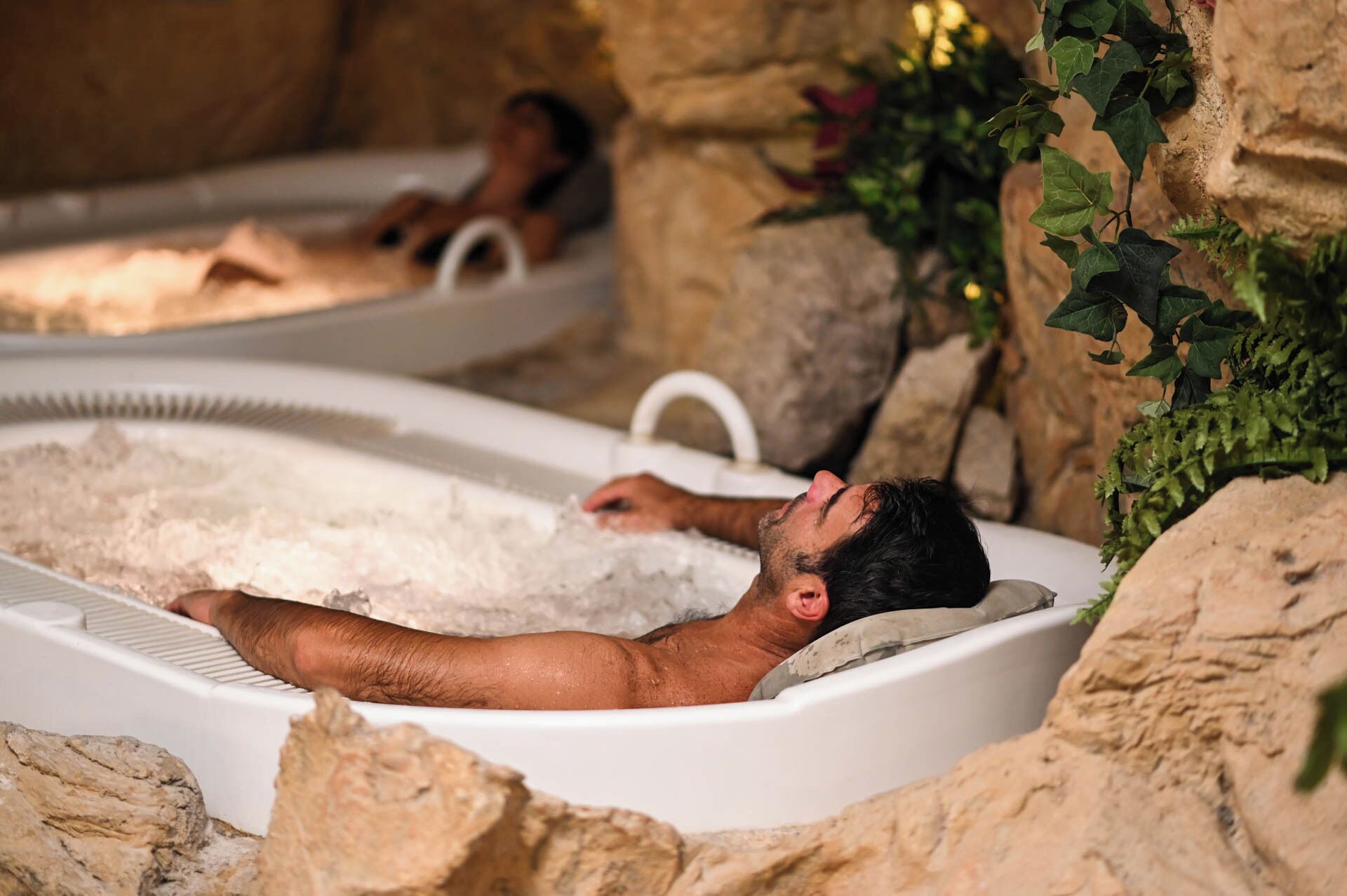 Two hot tubs in a natural setting with rocks and greenery.