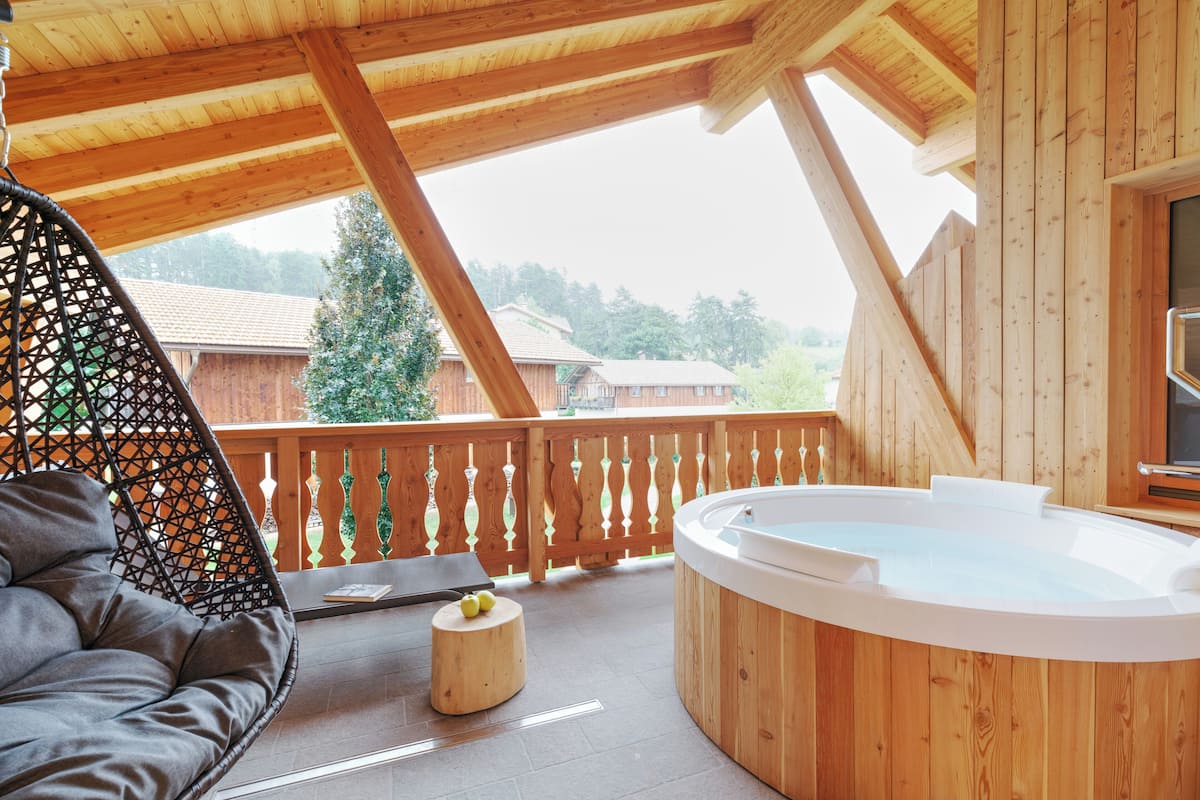 Une terrasse en bois avec un jacuzzi, un fauteuil confortable et une petite table ronde sur laquelle sont posées des pommes.