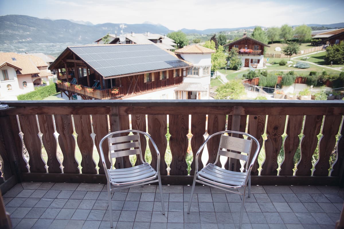 Un balcon avec deux chaises en métal et une vue sur un village, avec des maisons et des montagnes en arrière-plan.