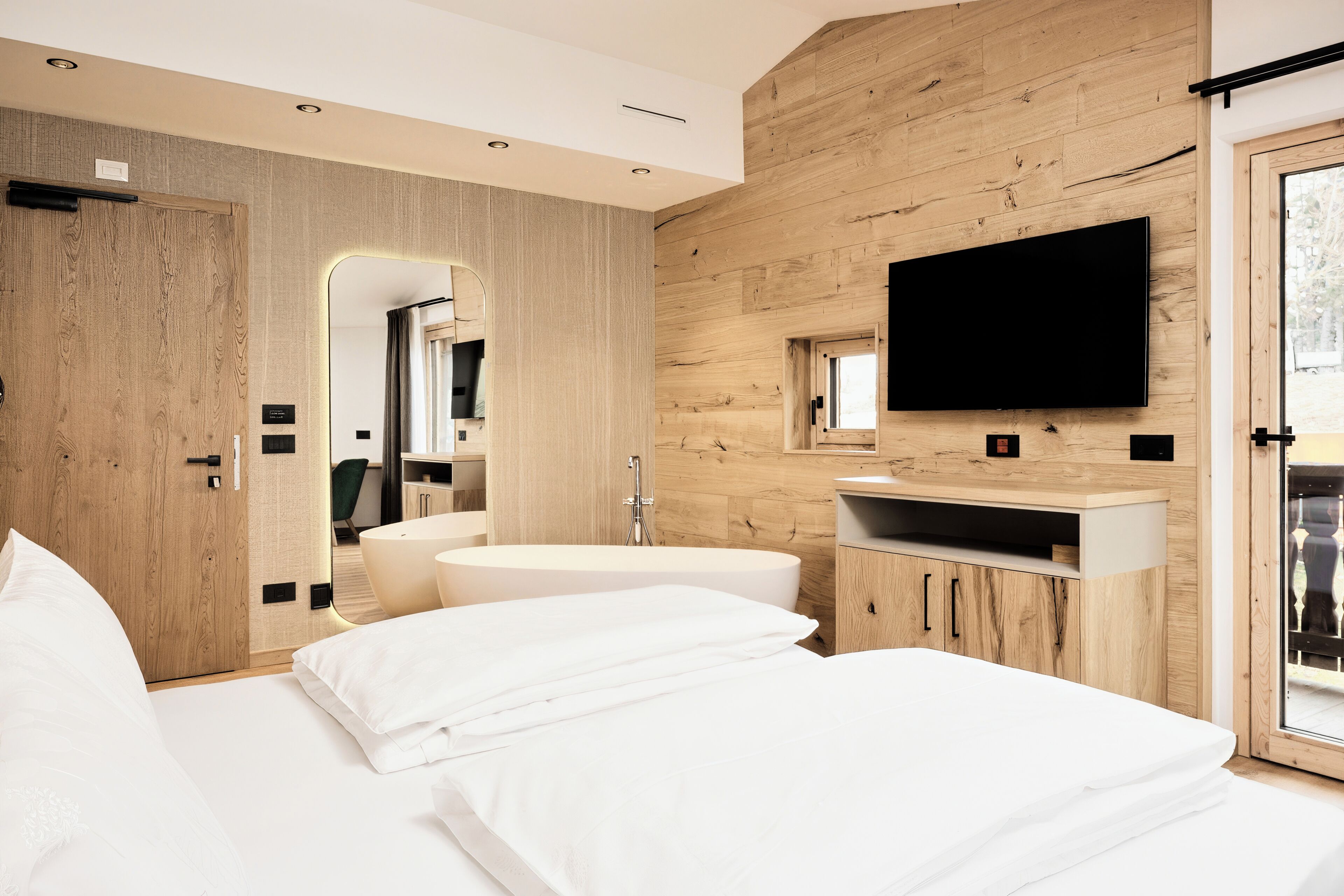 A modern bedroom with a wooden wall, a flat-screen TV, a large bed, and a built-in sink.