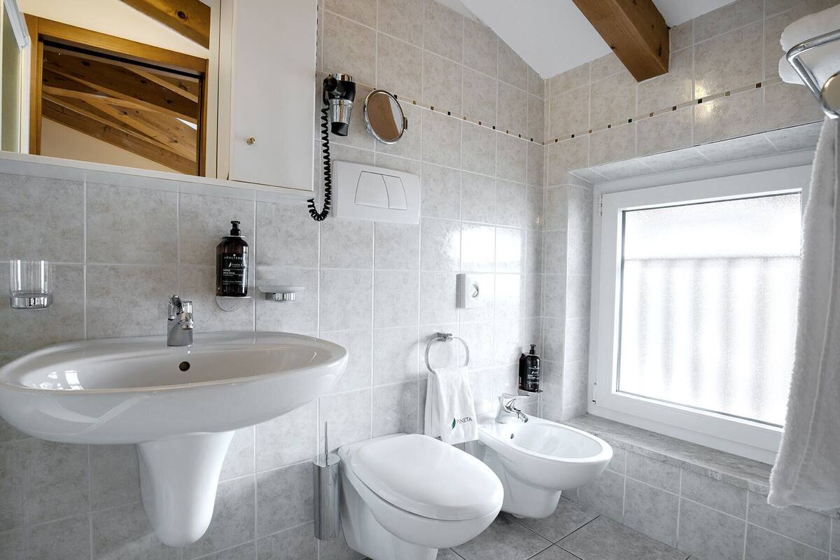 Une salle de bain avec un grand lavabo, des toilettes, un bidet et une fenêtre donnant sur un beau paysage.