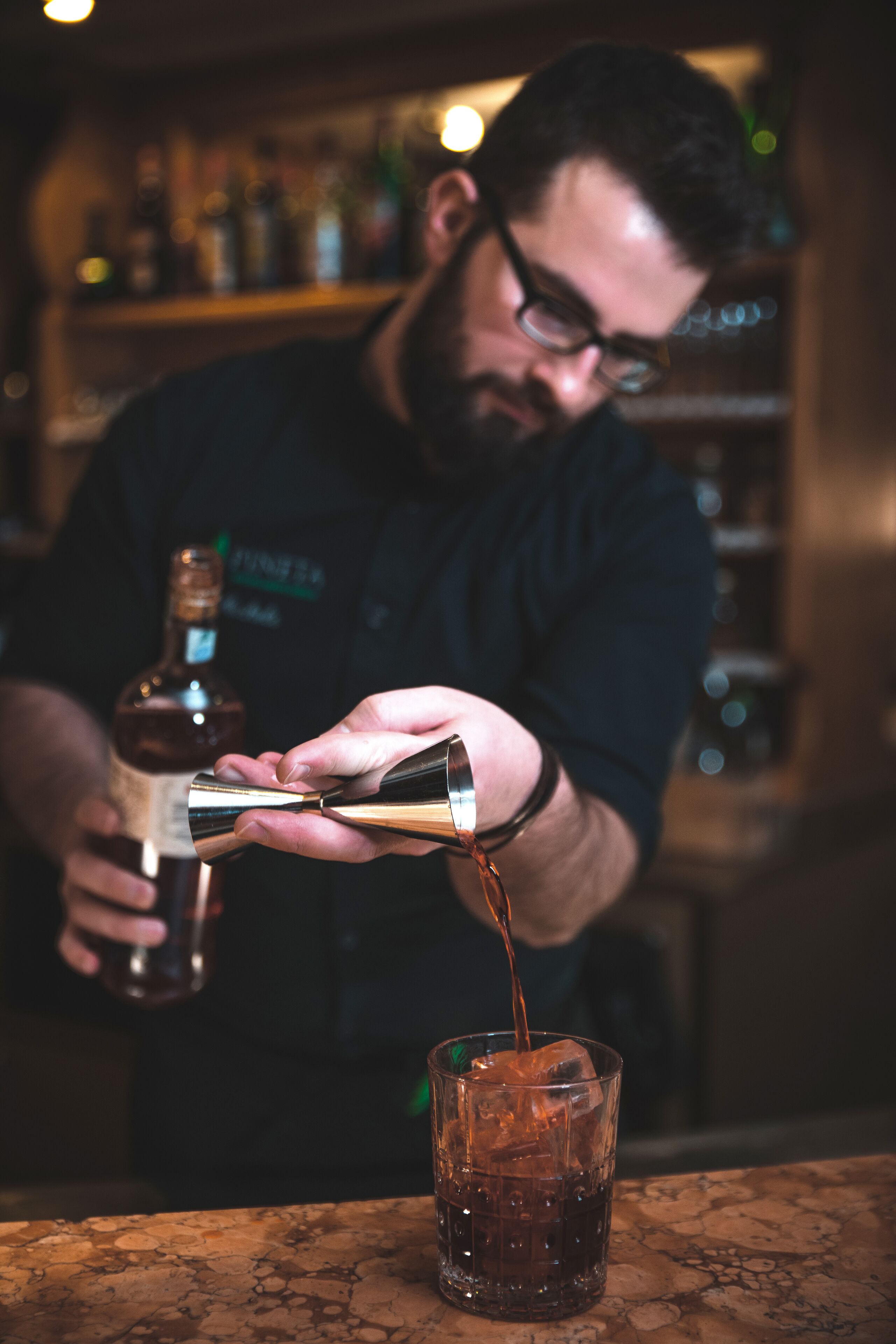 Eine Person gießt eine dunkle Flüssigkeit in ein Glas mit Eiswürfeln.