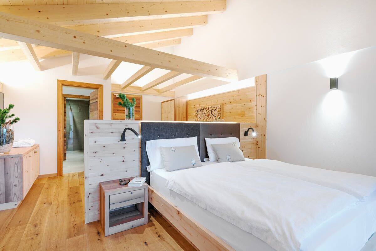 Une chambre avec un plafond en bois, un lit avec une literie blanche, une table de chevet et une lampe fixée au mur.