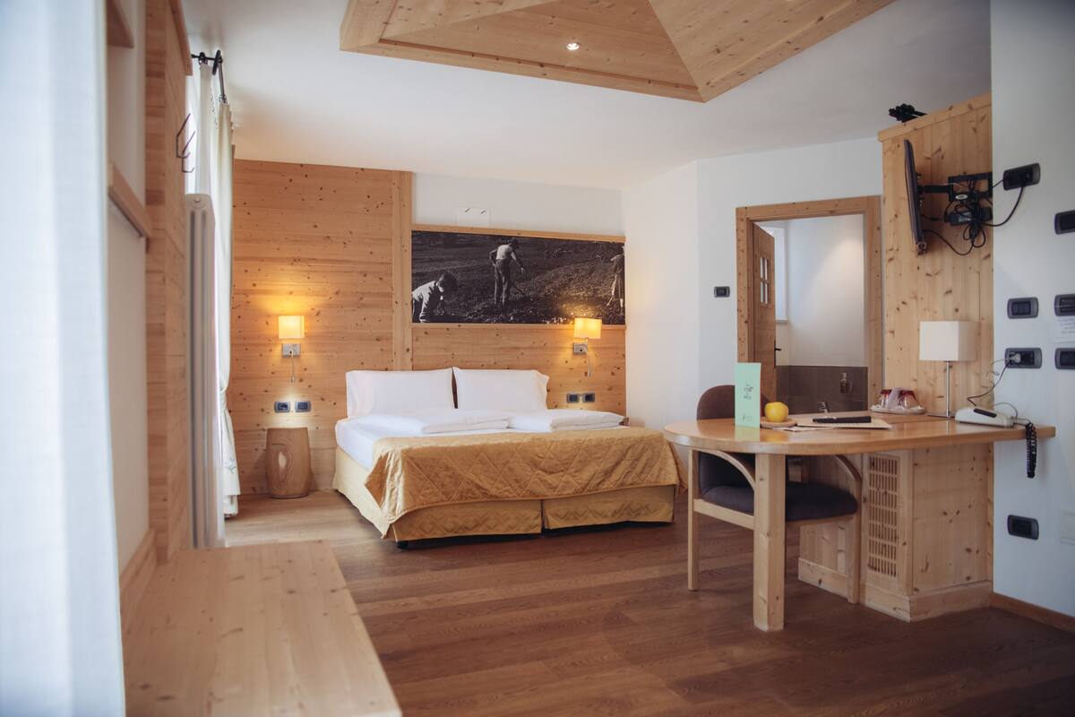 Une pièce aux murs lambrés, comprenant un lit, un bureau et un téléviseur fixé au mur.