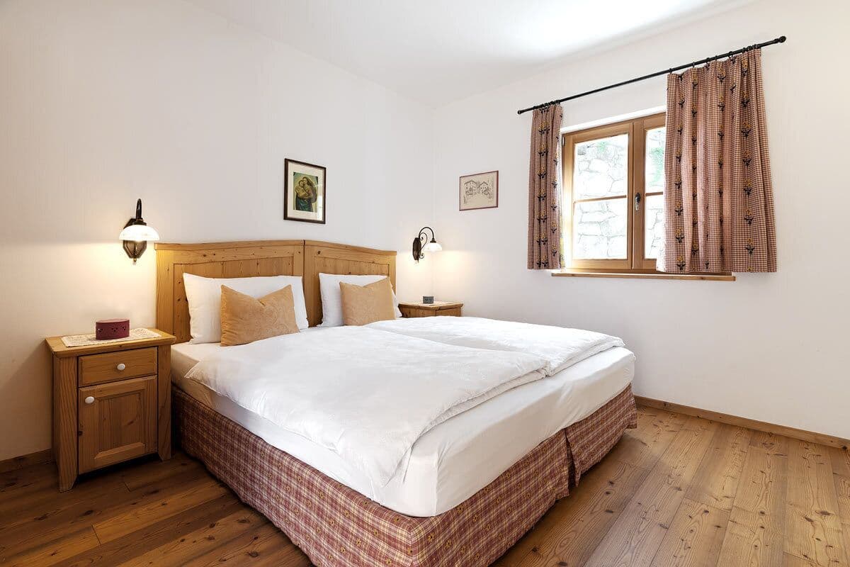 Une chambre à coucher avec un lit en bois, deux tables de chevet, une commode, une fenêtre avec des rideaux et des lampes fixées au mur.