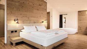 A modern bedroom with a wooden headboard, a large bed with white linens, a bedside table, and a built-in bathtub.