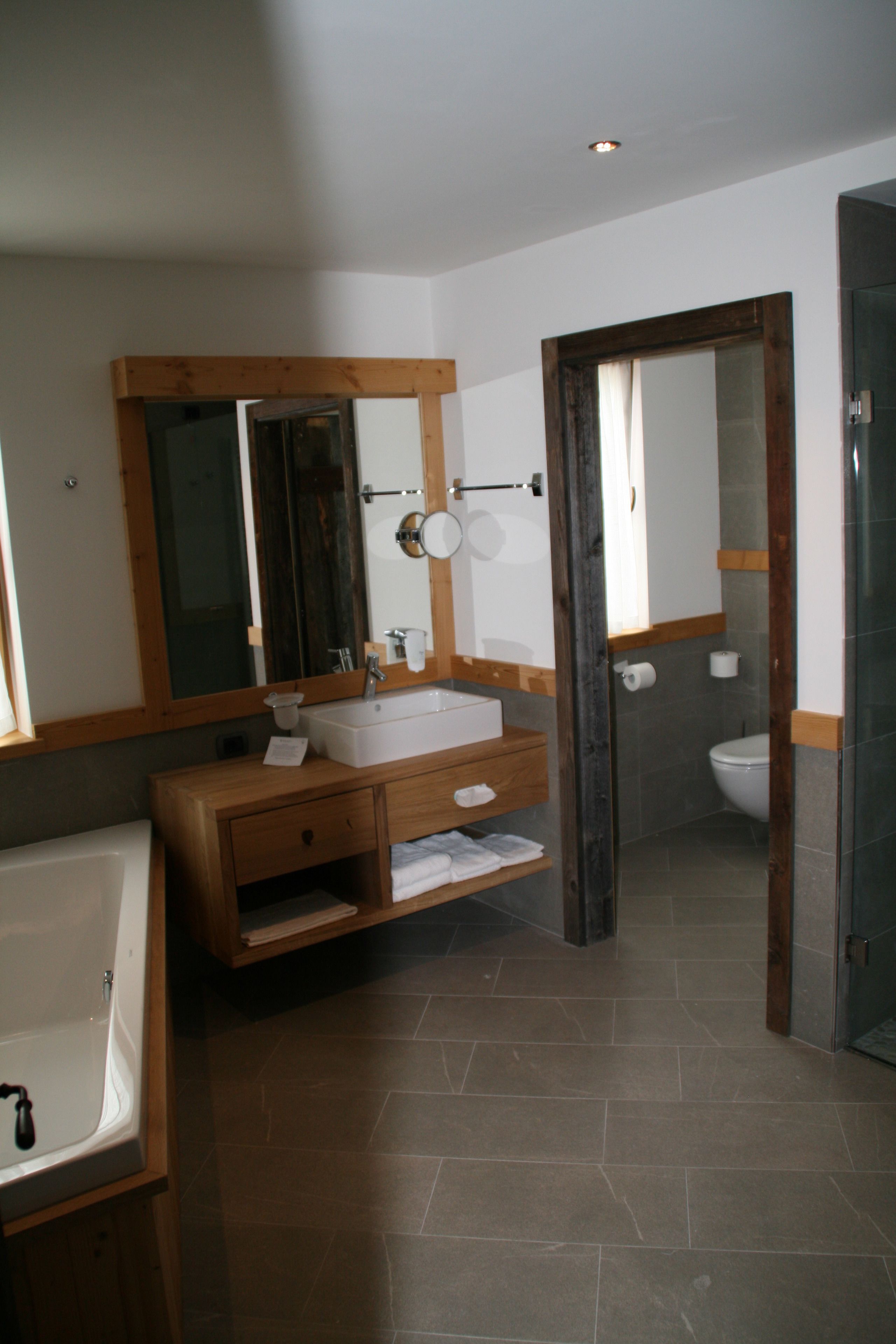 A bathroom with a wooden vanity, a white sink, a mirror, a toilet, and a shower area.