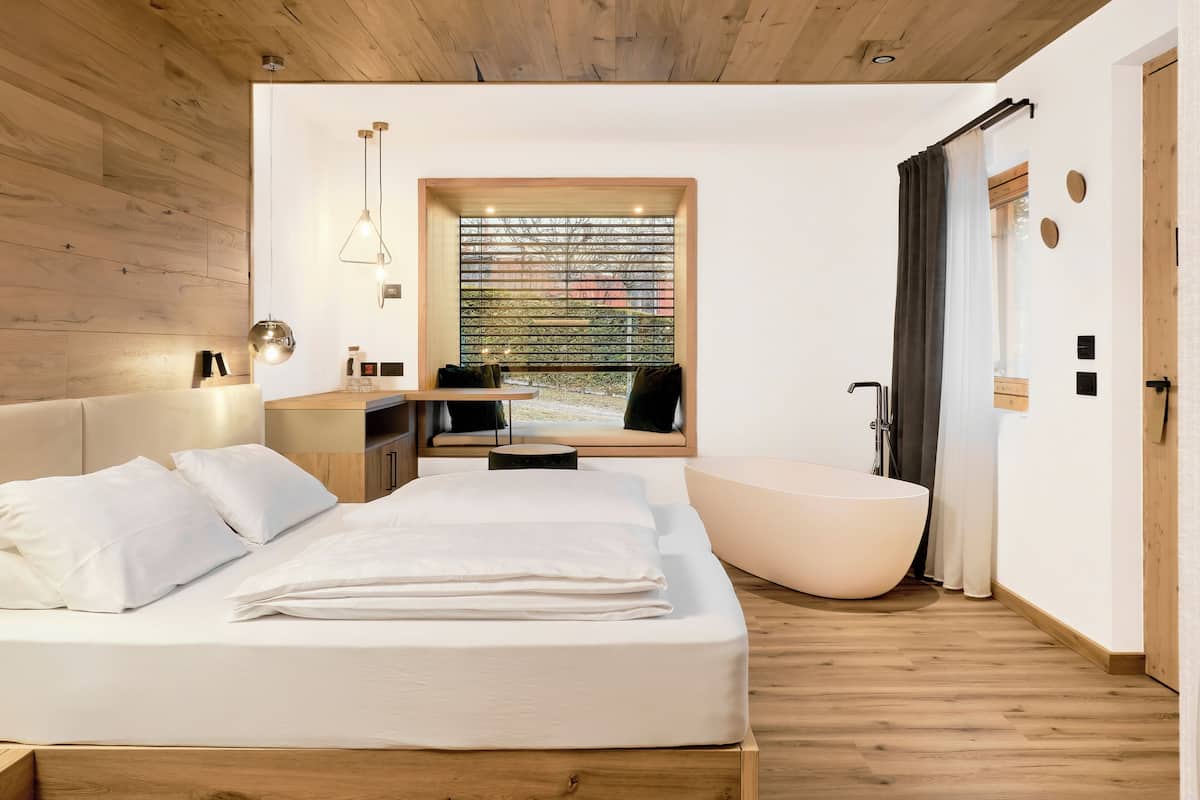 Une chambre moderne dotée d’un grand lit, d’un coin salon, d’une baignoire et d’une fenêtre offrant une vue agréable.