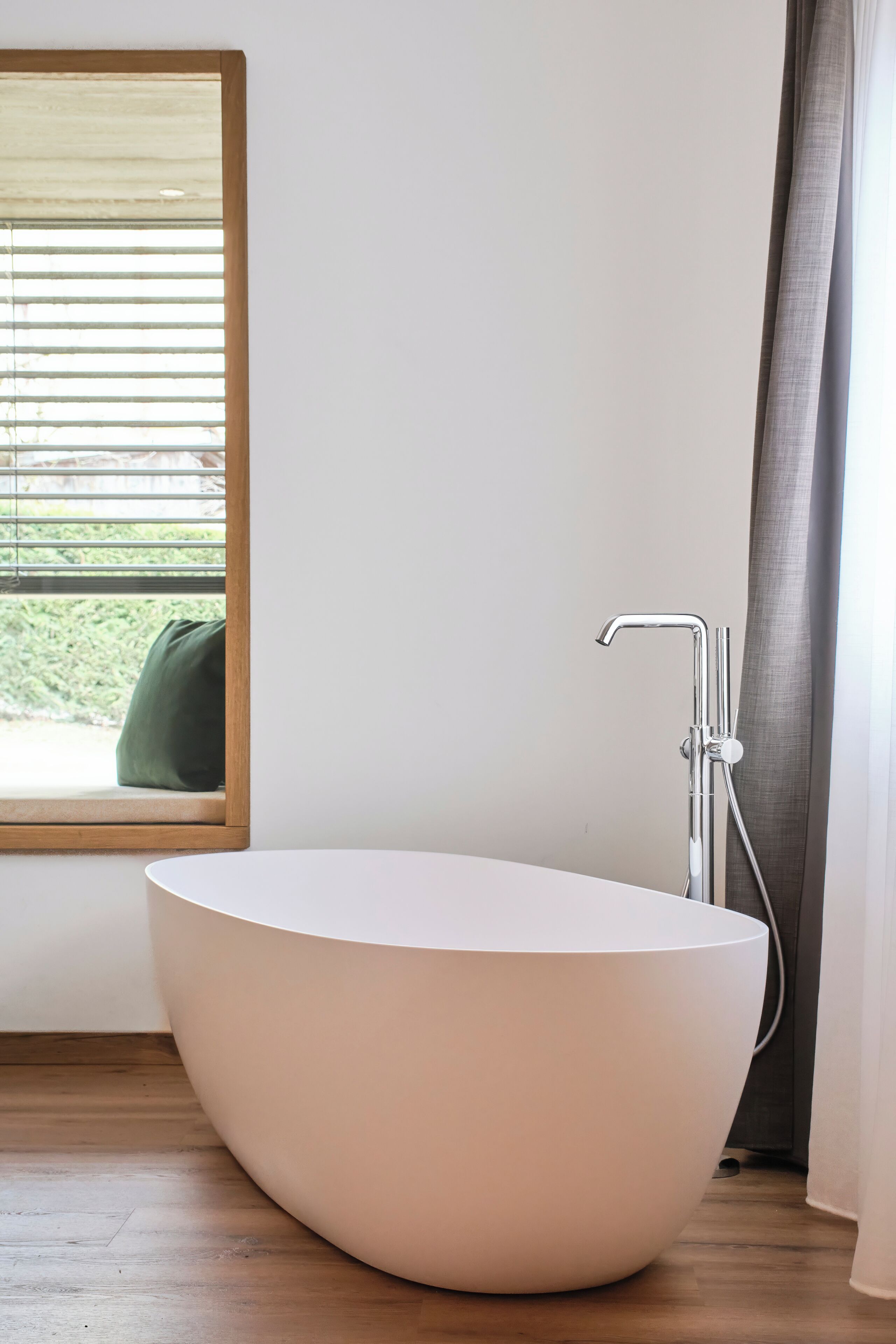 Un baño moderno con una bañera independiente, una ventana con persianas y vistas al exterior.