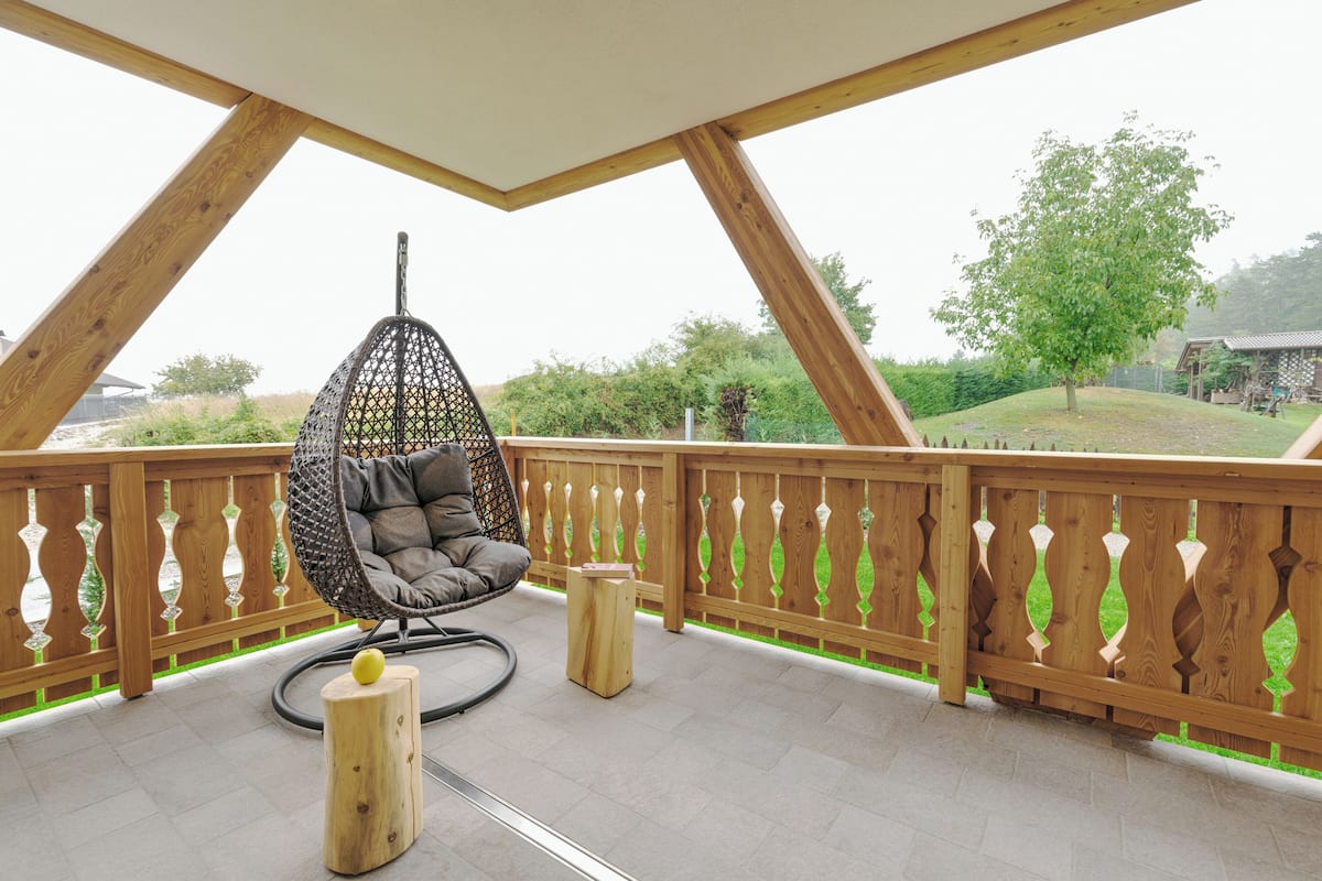 Une terrasse en bois avec un fauteuil suspendu, un petit tabouret et un poteau en bois sur lequel est posé un objet jaune.