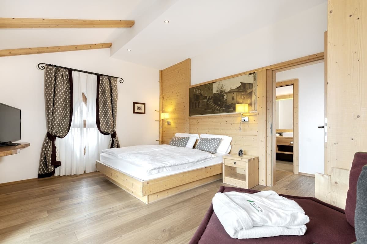 Une chambre à coucher avec un lit en bois, une télévision, un tableau, et une salle de bain visible à travers une porte ouverte.