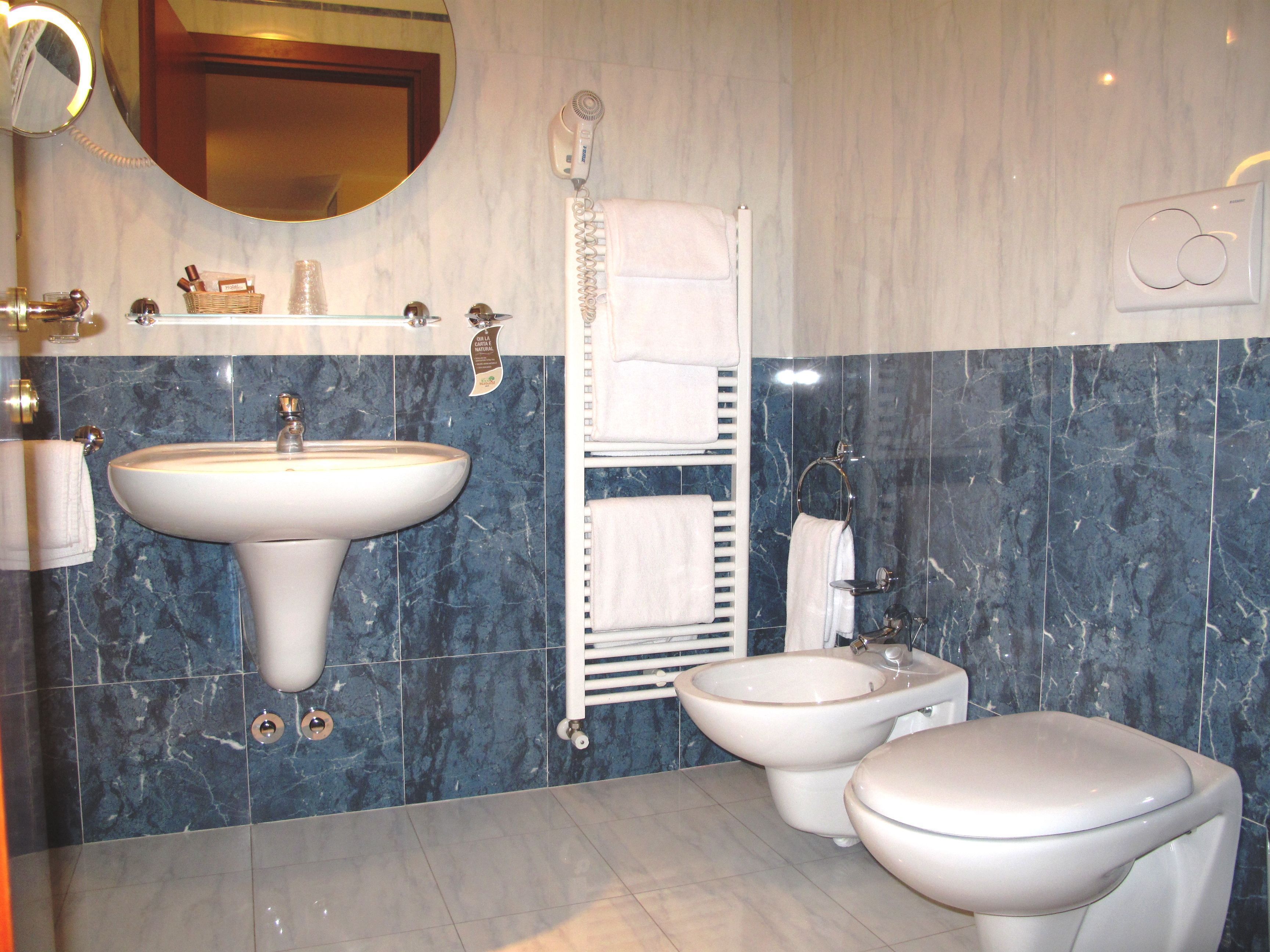 Un baño con lavamanos, bidé e inodoro, paredes de mármol y un perchero para toallas.