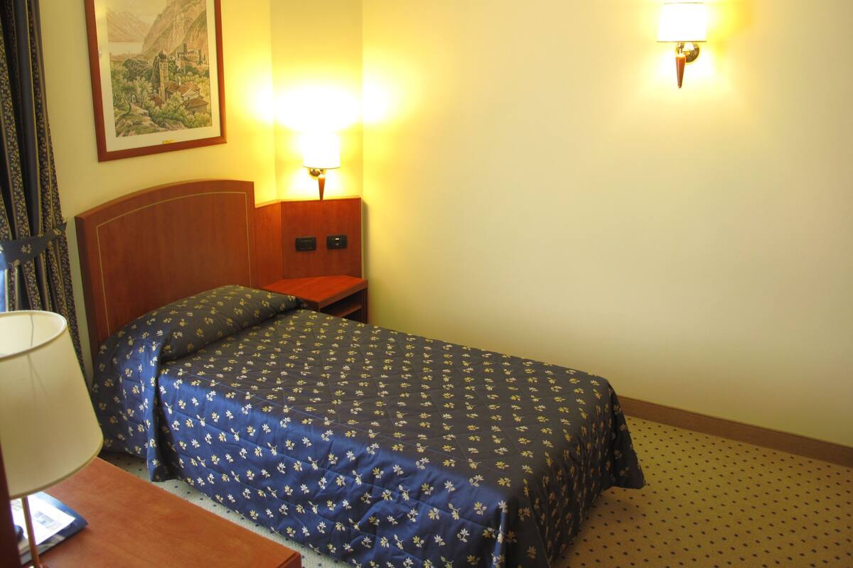 A hotel room with a bed, a nightstand, a lamp, and a wall-mounted light fixture.