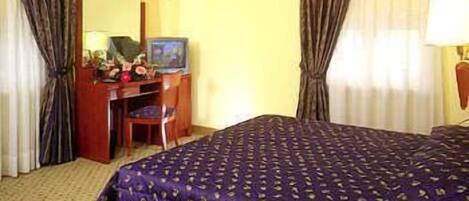 Een hotelkamer met een bed, een bureau, een stoel, een televisie en gordijnen.