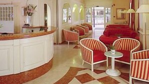 Un vestíbulo de hotel con una recepción de forma curva, sillones a rayas, un sofá rojo y un suelo estampado.