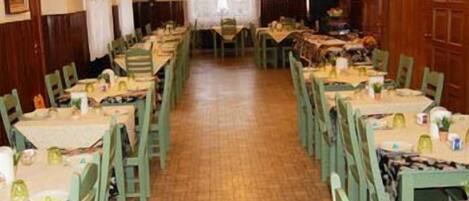 A dining area with rows of tables and chairs, a wooden floor, and a window with curtains.