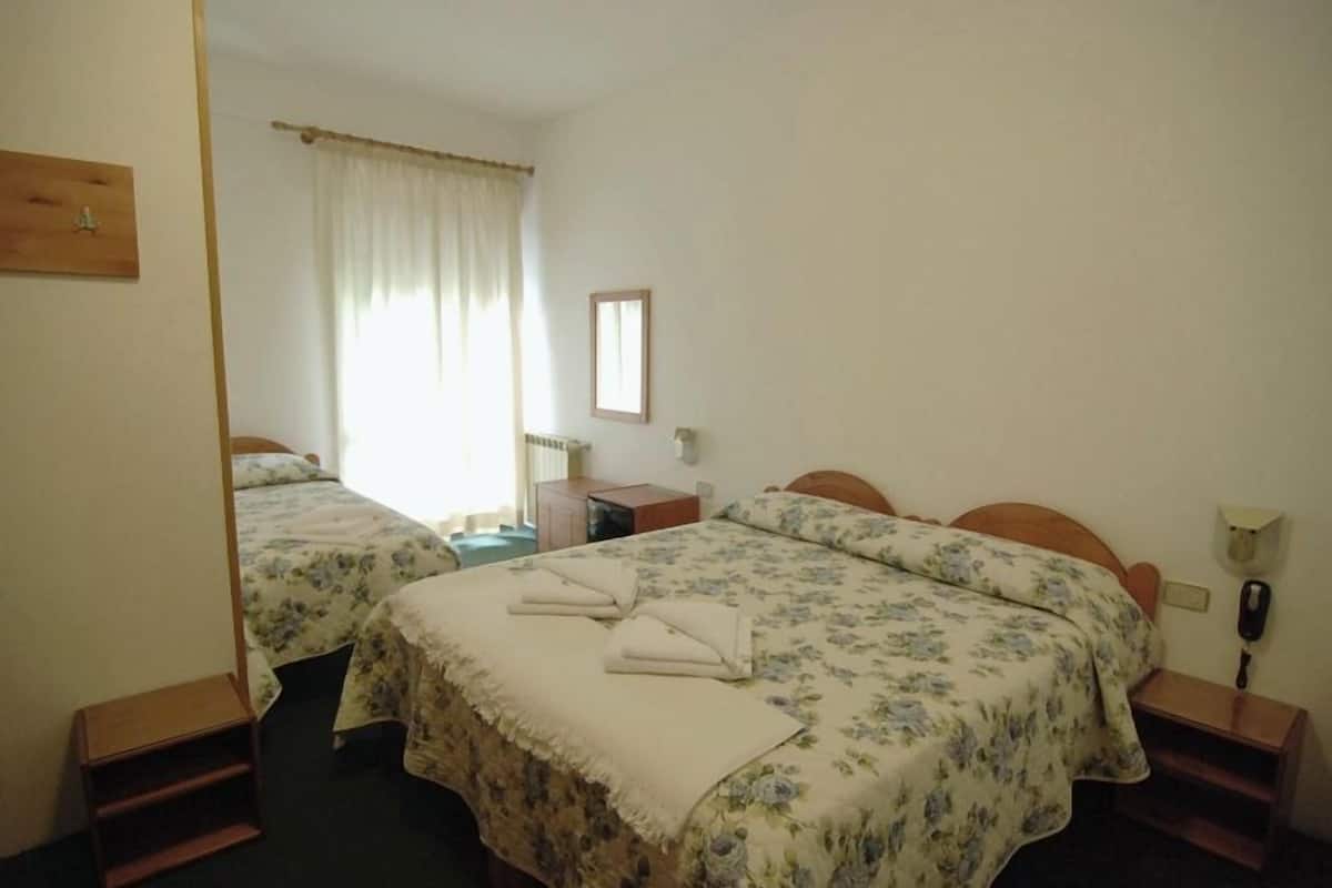 A hotel room with two beds, a small desk, a chair, a telephone, and a window with curtains.
