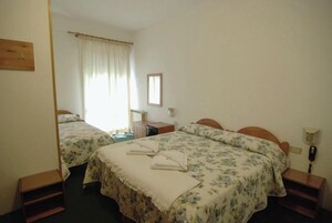 Una camera d'albergo con due letti, una scrivania, una sedia, un telefono e una finestra con tende.