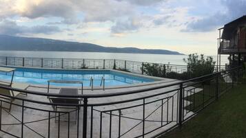 Una piscina de diseño curvo, rodeada por una valla metálica, con vistas a una masa de agua y montañas al fondo.