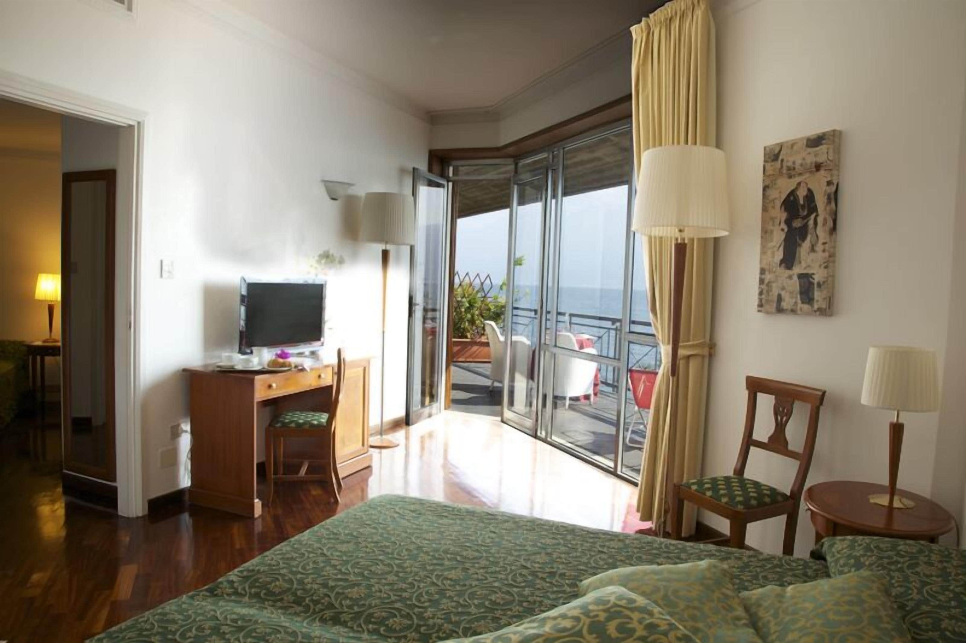 Une chambre d’hôtel avec un lit, un bureau avec un ordinateur, une chaise, une petite table et un balcon avec vue.