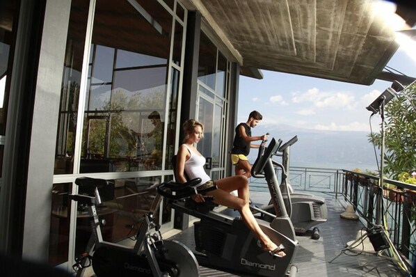 Un gimnasio equipado con máquinas de ejercicio, incluyendo una cinta de correr y bicicletas estáticas, con amplias ventanas que ofrecen vistas al exterior.