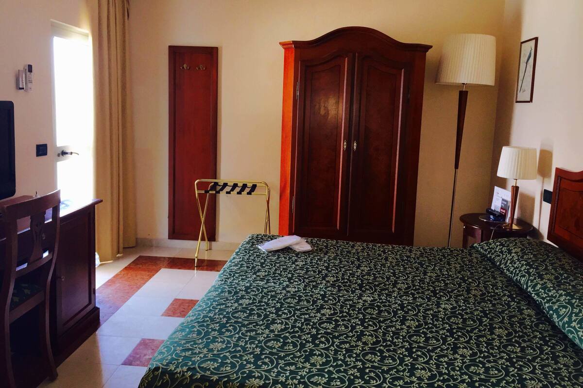 Una habitación de hotel con cama, armario, escritorio y lámpara.