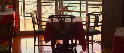 A dining area with a table and chairs, large windows with a view of the sea, and a wooden floor.