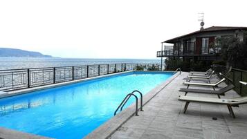 Une piscine avec vue sur la mer, un balcon avec des chaises longues et un immeuble équipé d’une antenne parabolique.