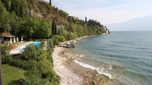 A coastal landscape with a swimming pool, a wooden pier, and a hillside with trees. - Villa Cappellina (Toscolano Maderno)