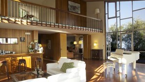 A spacious living area with a piano, a white sofa, and a bar area with stools. - Villa Cappellina (Toscolano Maderno)