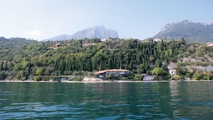 A lakeside property with a large house and several smaller buildings, surrounded by dense greenery and mountains in the background. - Villa Cappellina (Toscolano Maderno)