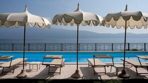 A poolside area with lounge chairs and umbrellas, a clear view of the sea, and a railing in the background. - Villa Cappellina (Toscolano Maderno)