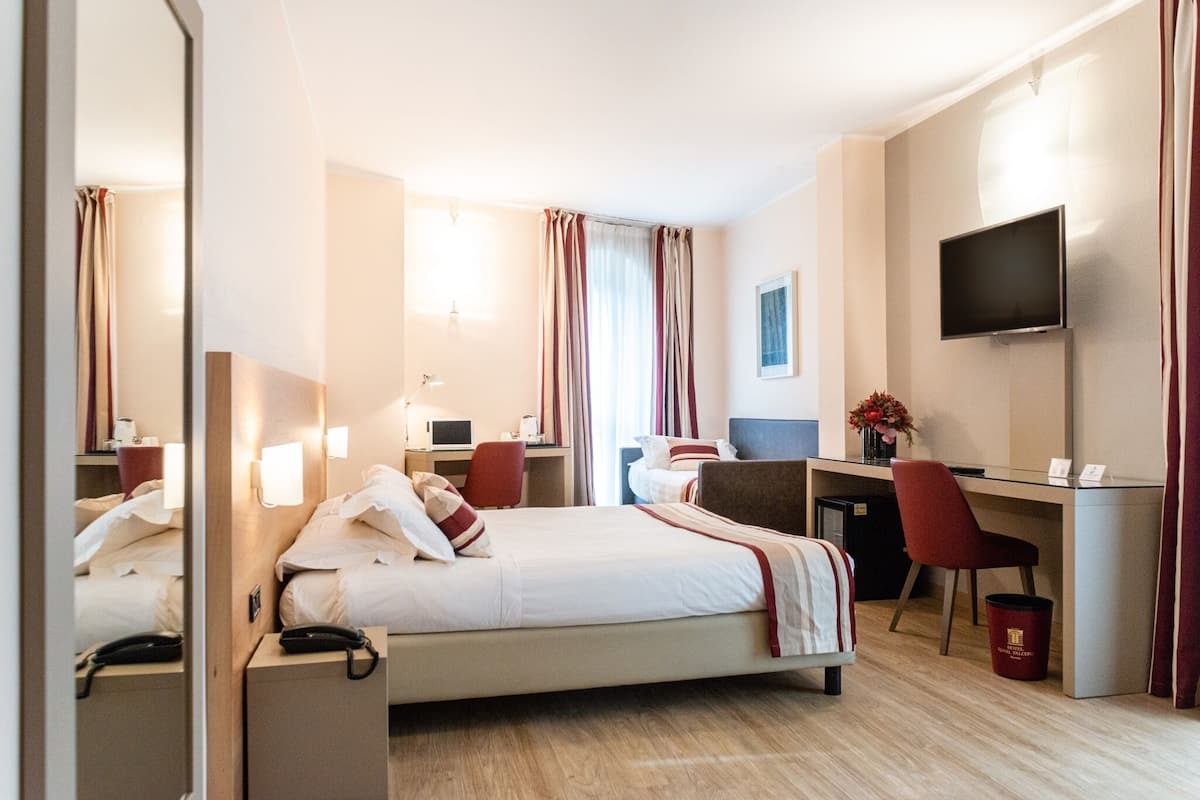 A hotel room with a bed, desk, chair, TV, and a small trash bin.