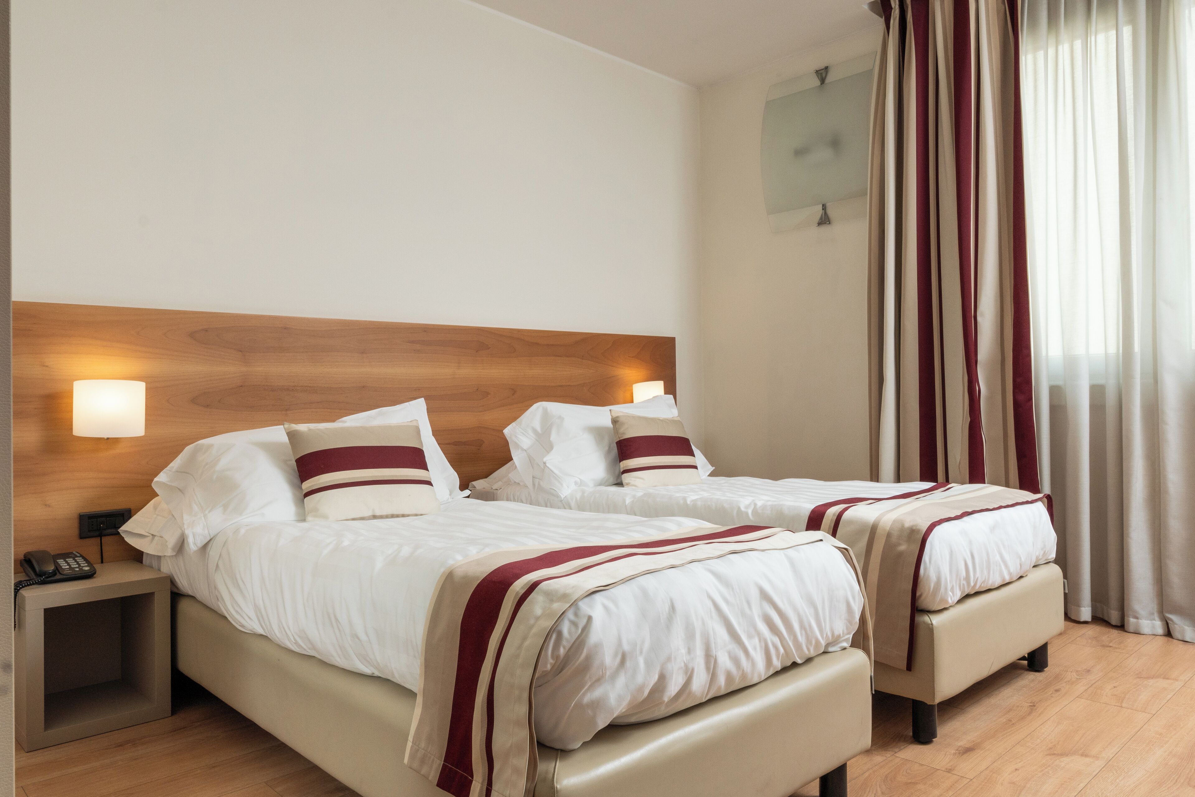 Ein Hotelzimmer mit zwei Betten, einem Holz-Kopfteil, Nachttischlampen und einem Telefon auf dem Nachttisch.