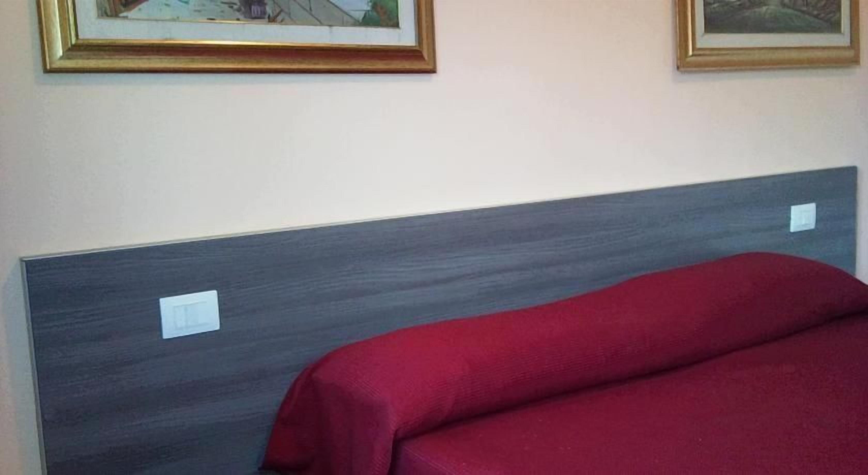 Una cama con cabecera gris y colcha roja en una habitación con dos cuadros en la pared.