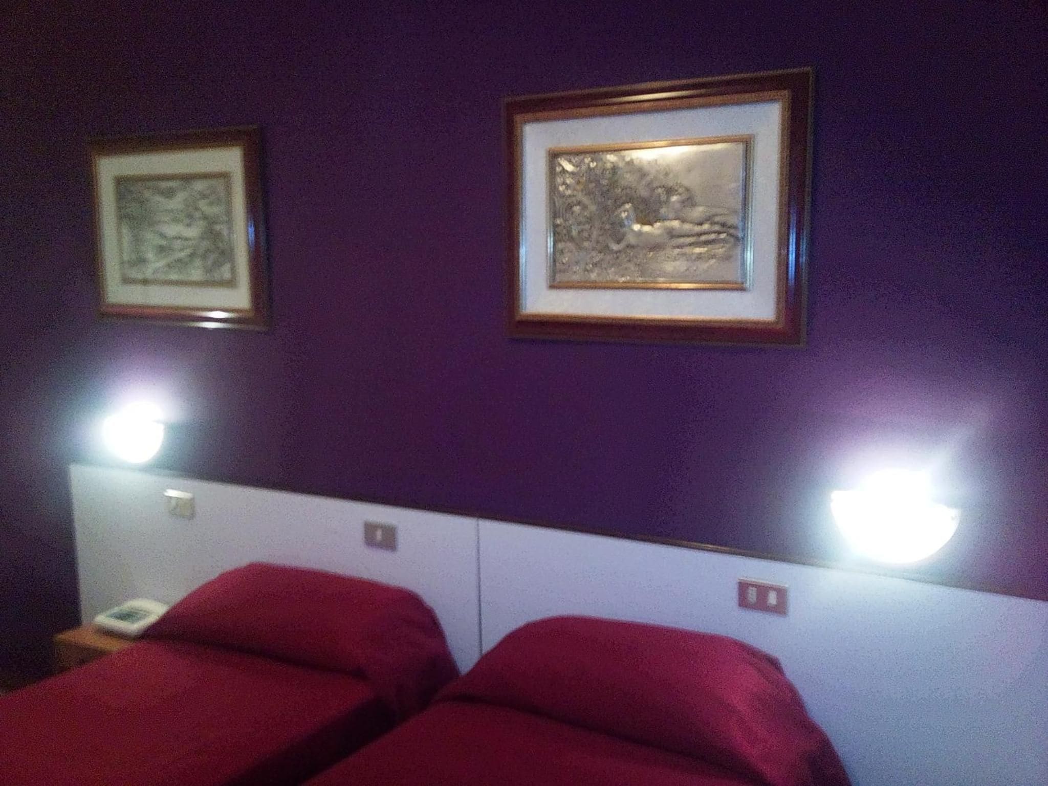 A hotel room with two beds, a white headboard, purple walls, and two framed pictures.
