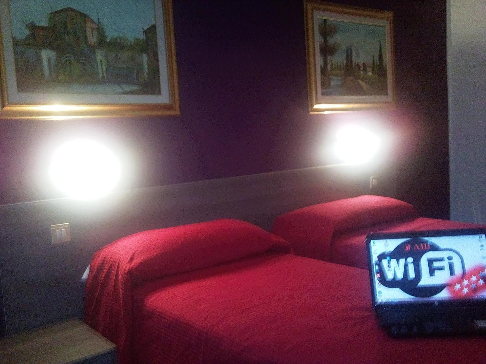 Ein Hotelzimmer mit zwei Betten, einem Laptop der ein WLAN-Symbol anzeigt und zwei gerahmten Bildern an der Wand.